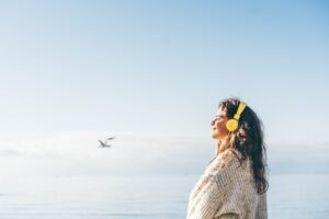 Young woman listening music with headphones on the beach in winter.