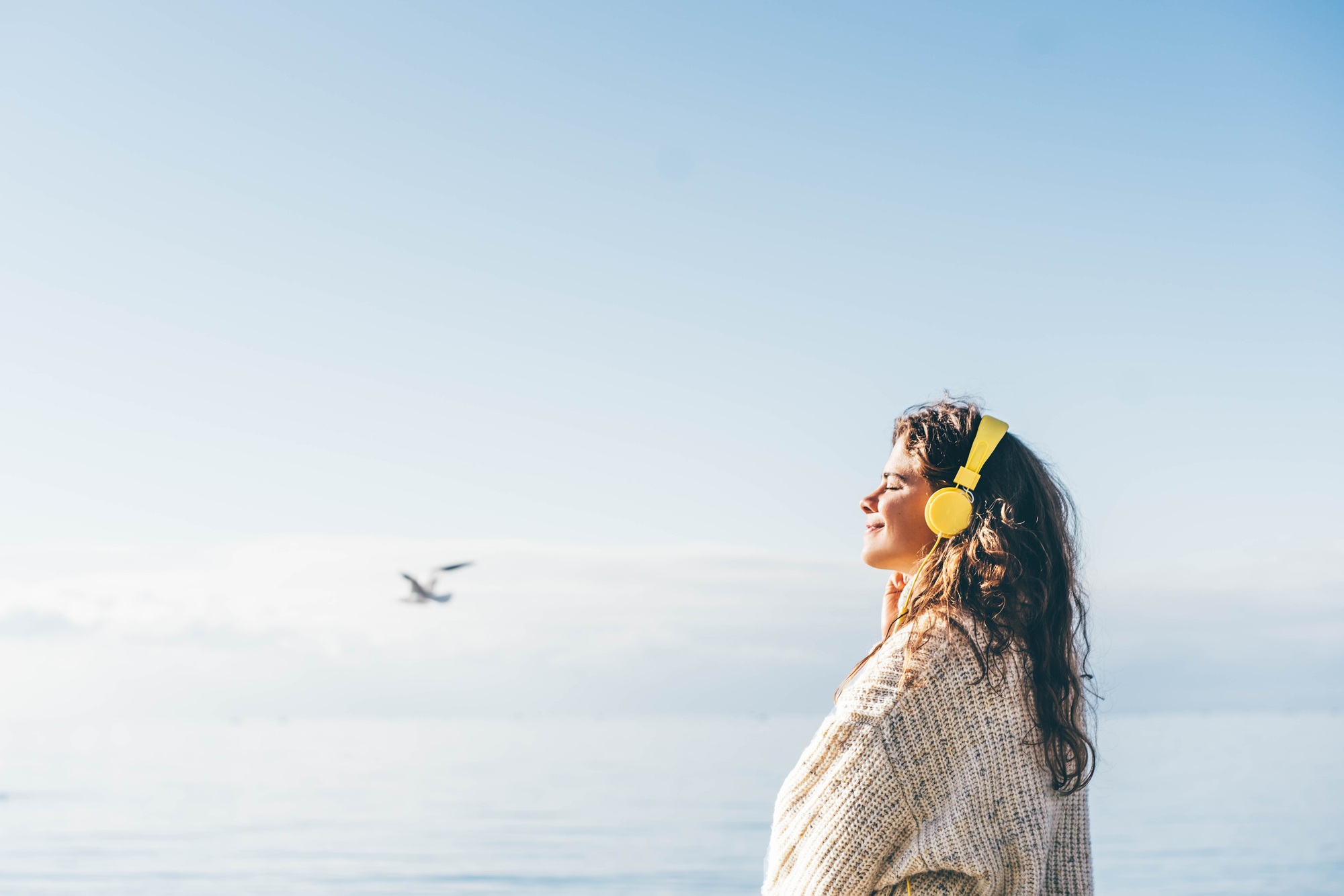 Young woman listening music with headphones on the beach in winter.